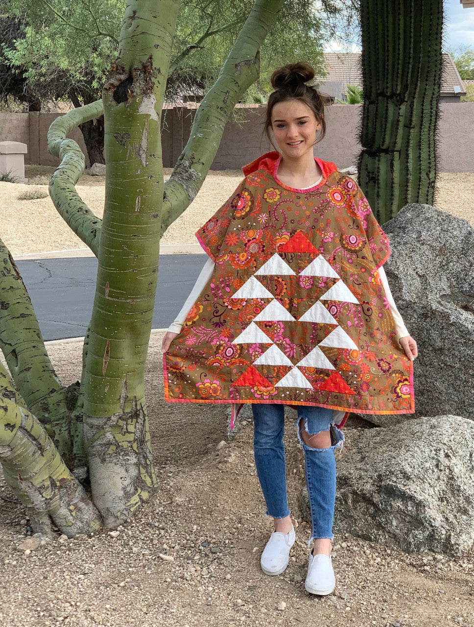 Person wearing a colorful quilted poncho standing outdoors with trees and rocks in the background