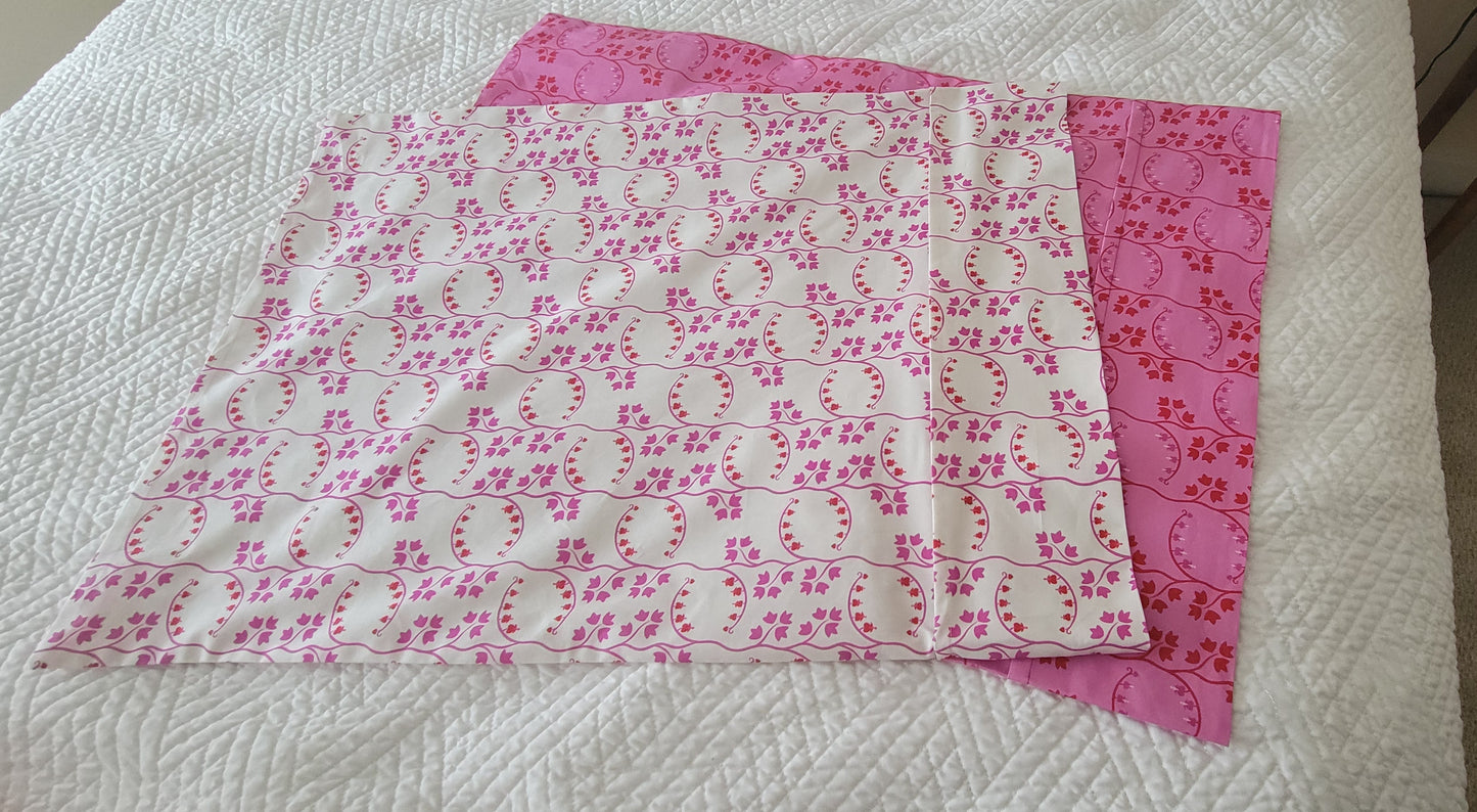 Two coordinating pillowcase fabrics laid flat on a white quilted surface, showing pink and white prints.