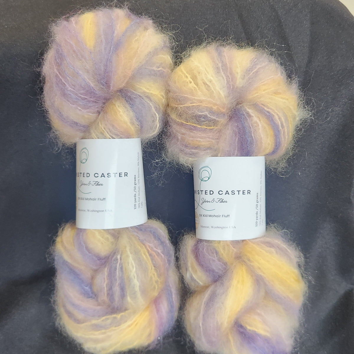 Four skeins of fluffy variegated yarn in Lavender & Yellow, arranged on a dark gray fabric background.