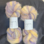 Four skeins of fluffy variegated yarn in Lavender & Yellow, arranged on a dark gray fabric background.