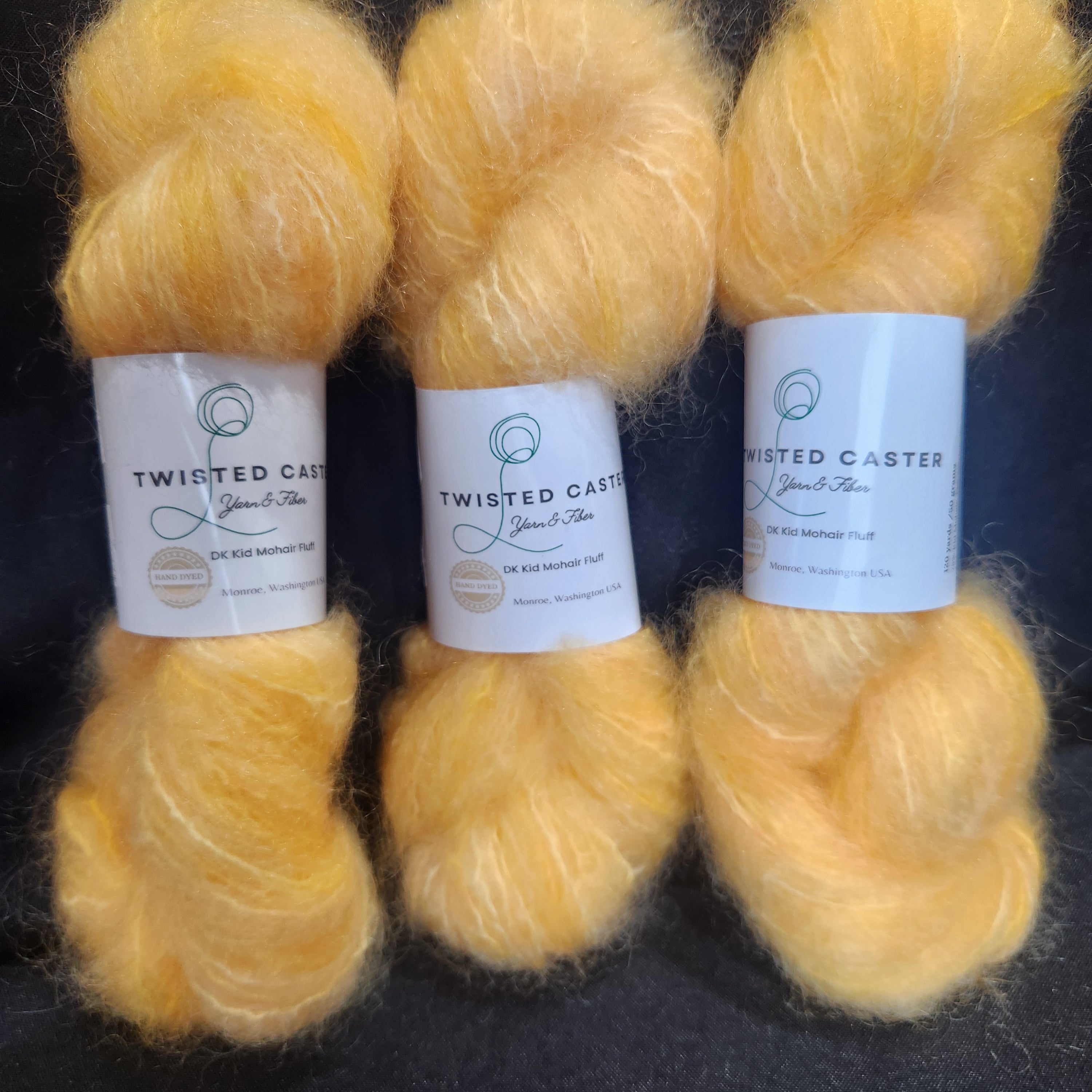 Three skeins of fluffy yellow yarn with white paper labels, arranged vertically on a dark textured background.
