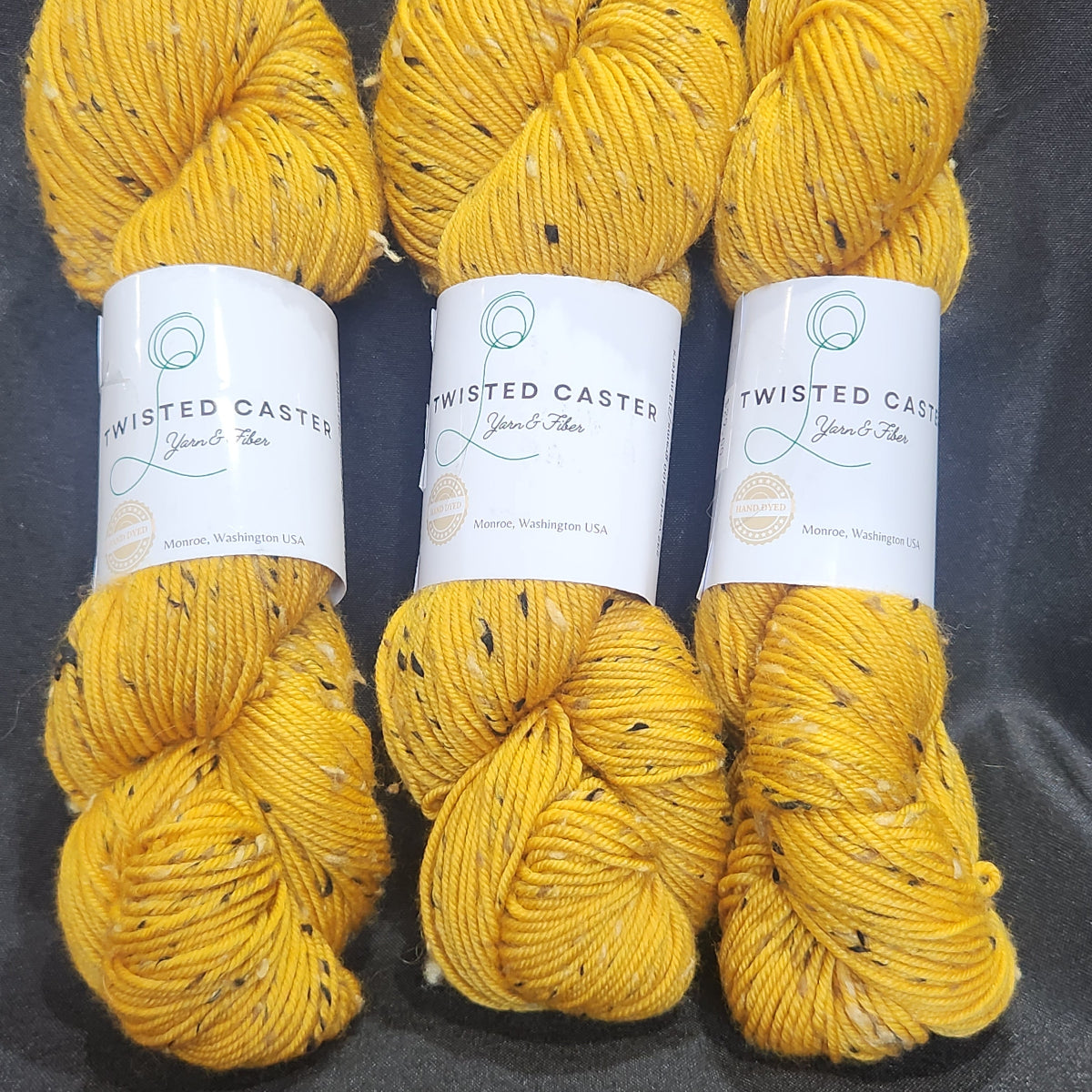 Three skeins of yarn in a golden yellow color with small black flecks.