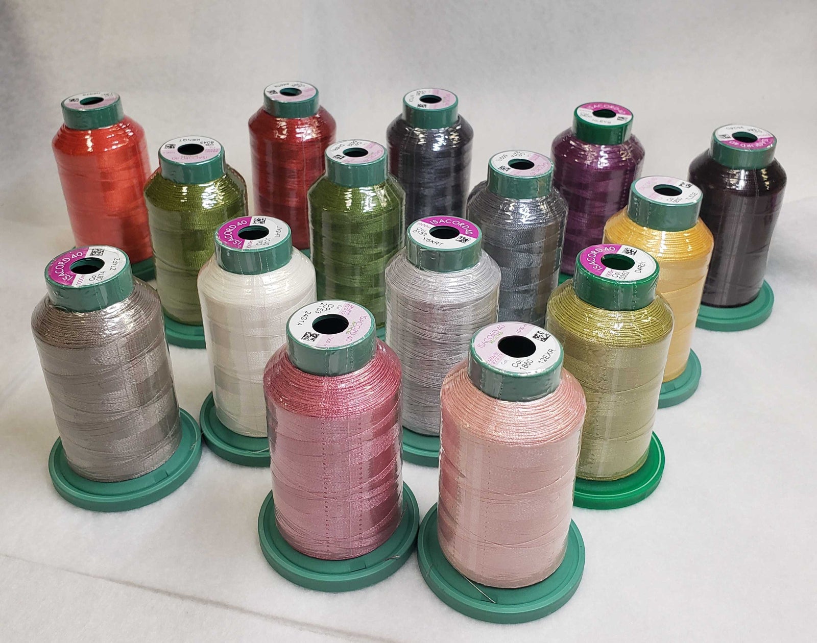 A collection of colorful spools of thread. The spools come in a variety of colors including red, green, purple, yellow, pink, and silver, each mounted on a green plastic base.