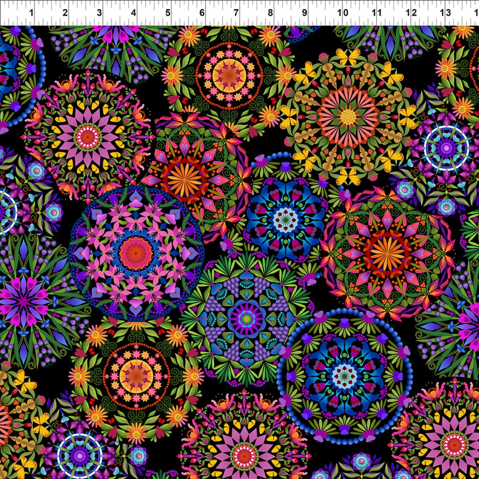 A close-up of a fabric pattern featuring colorful mandala and floral motifs on a black background, with a white ruler at the top showing measurement scale.
