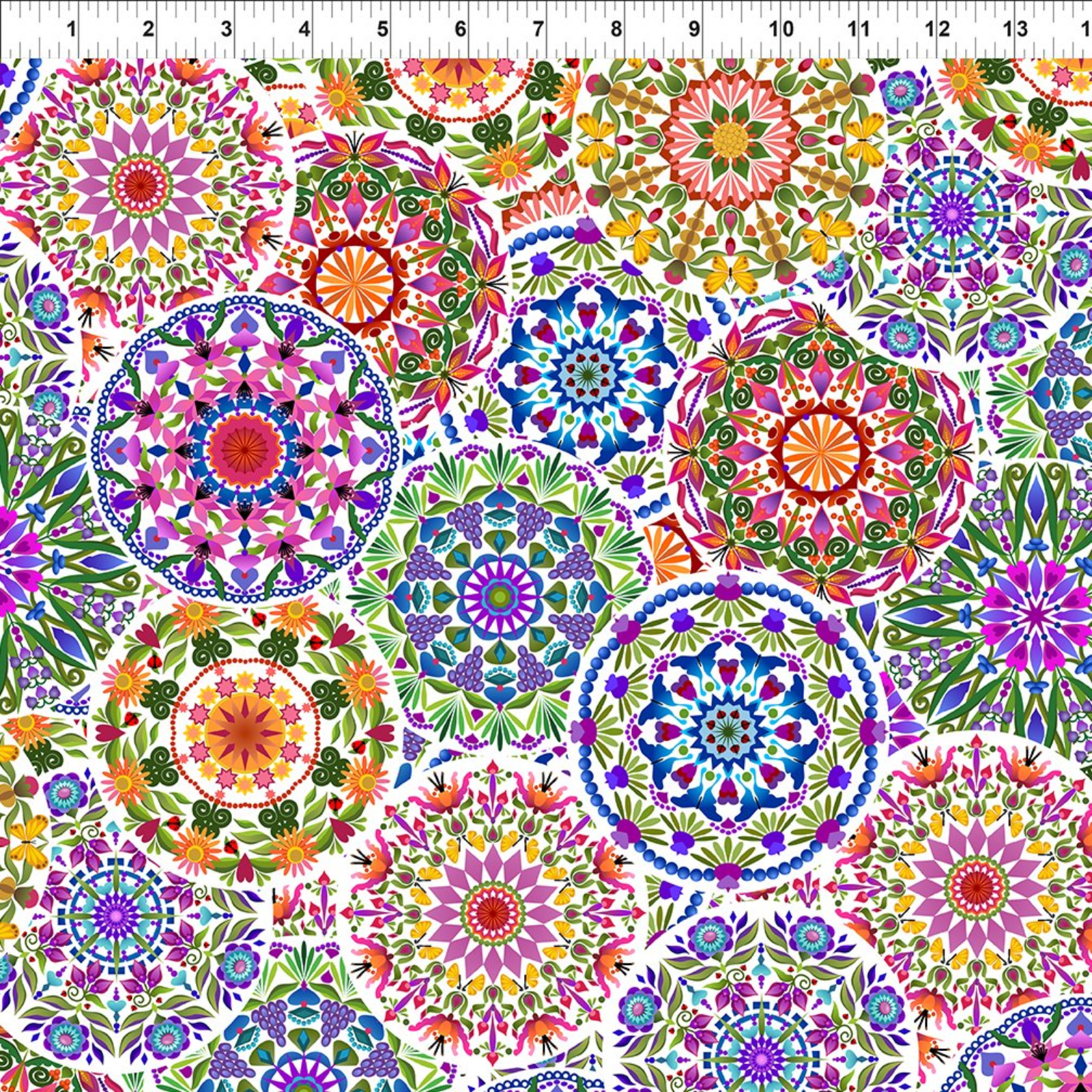 A close-up of a colorful fabric featuring repeating circular mandala and floral motifs in pink, purple, blue, green, orange, yellow, and red on a white background, with a ruler at the top showing scale.