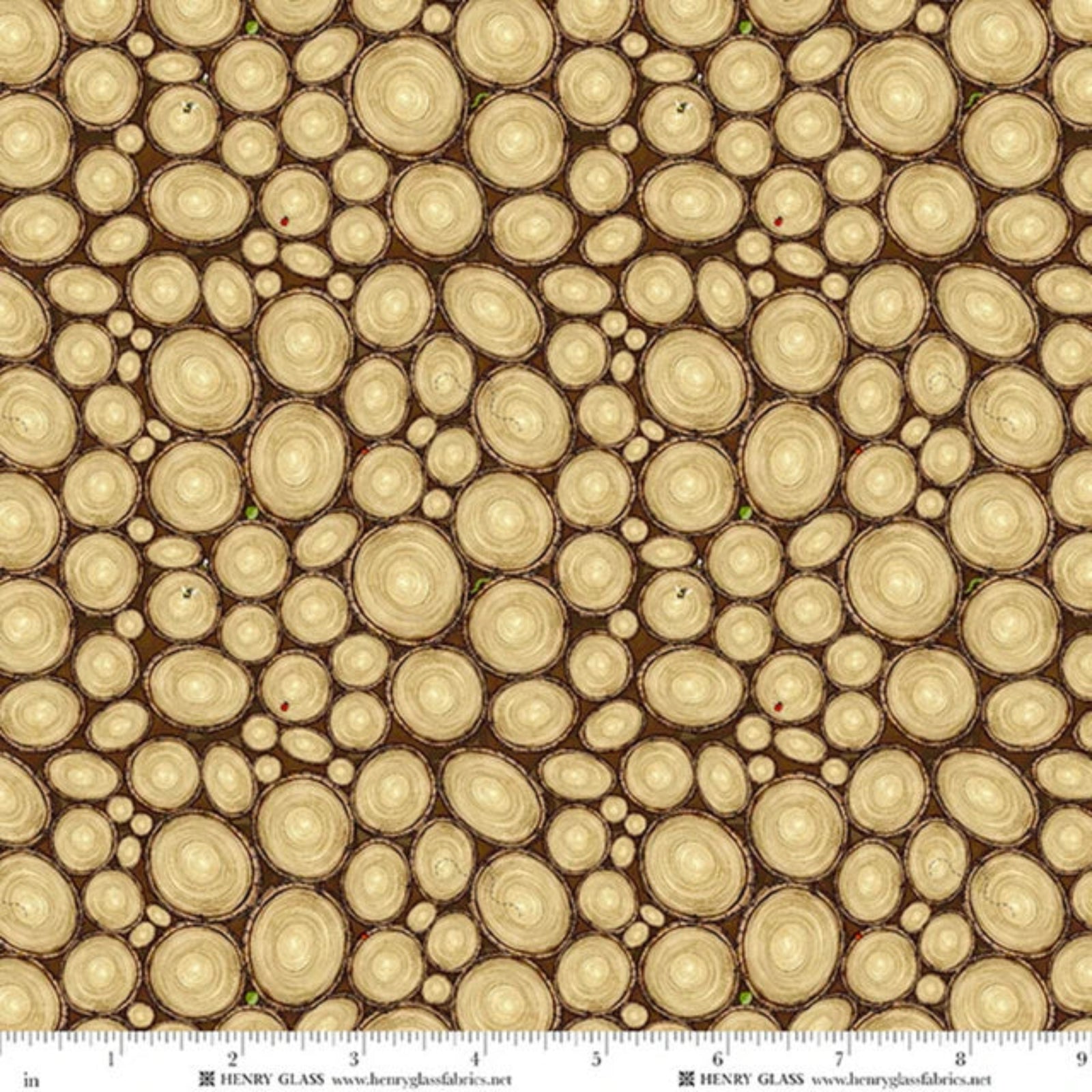 A repeating pattern of overlapping tree trunk cross-sections in warm beige and tan tones on a dark brown background, with a ruler scale and the brand name Henry Glass visible along the bottom edge.