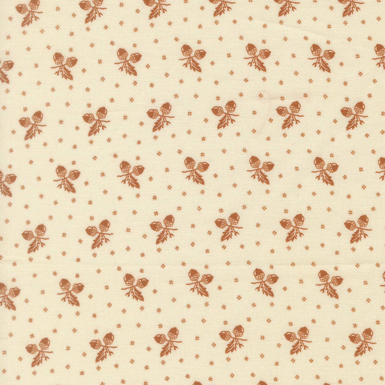 A close-up of a cream-colored fabric with a repeating brown pattern of small floral clusters and tiny diamond motifs.