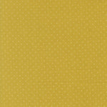 A close-up of a mustard yellow fabric with a repeating pattern of small white polka dots.