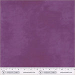 A close-up of a purple fabric swatch with a subtle woven texture, featuring a white ruler and Windham Fabrics branding along the bottom edge.