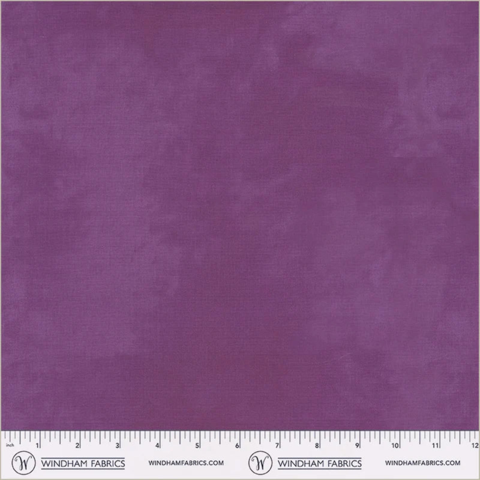 A close-up of a purple fabric swatch with a subtle woven texture, featuring a white ruler and Windham Fabrics branding along the bottom edge.