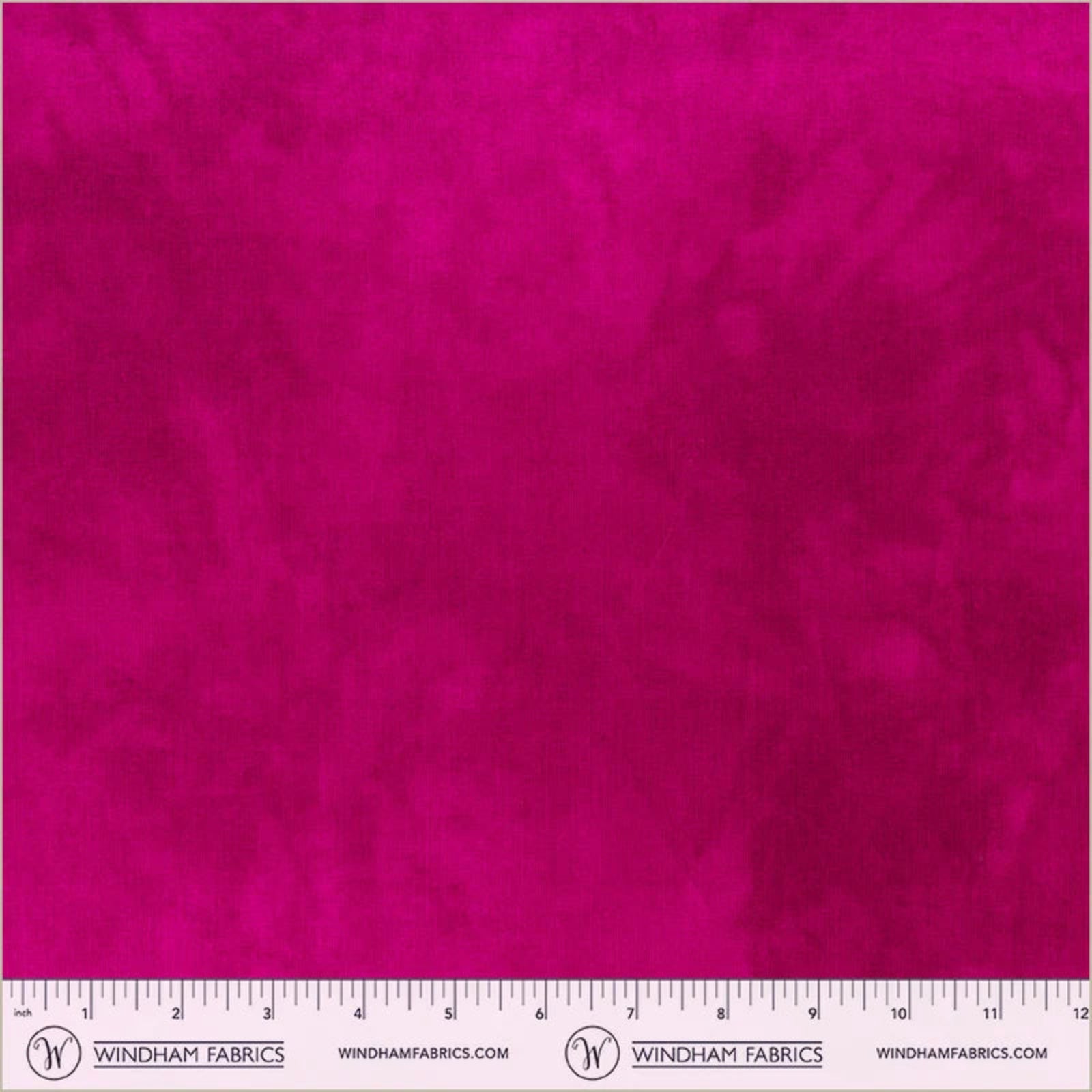A close-up of bright fuchsia pink fabric texture with a ruler along the bottom edge showing measurements. The brand name Windham Fabrics is printed on the ruler.