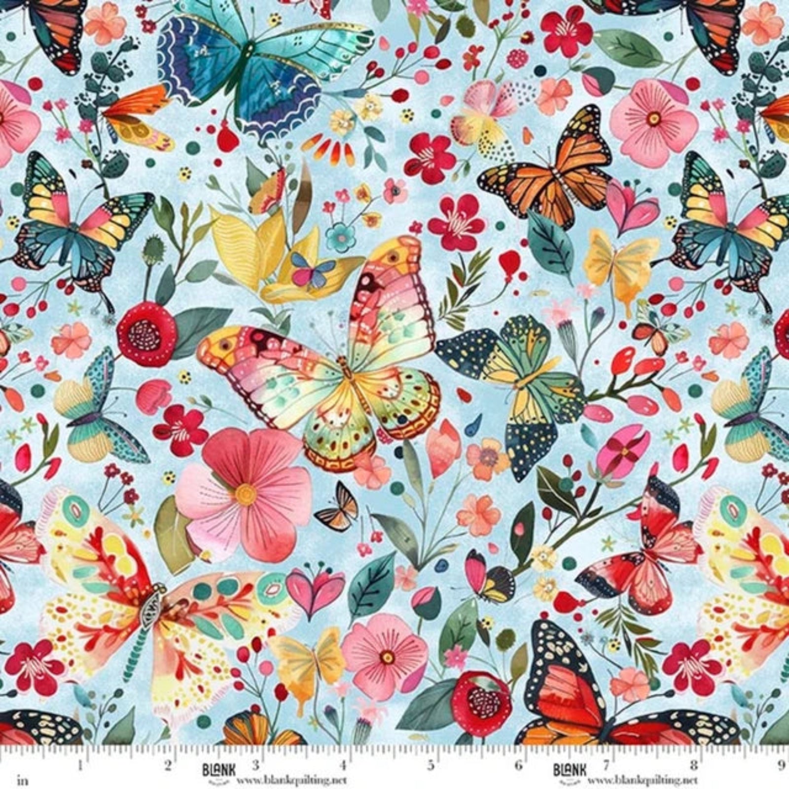 A close-up of a printed fabric pattern featuring colorful butterflies, flowers, leaves, and small birds on a pale blue background, with a measurement ruler along the bottom edge showing the scale of the print.