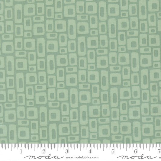 Patterned fabric with geometric shapes on a green background with a ruler for scale