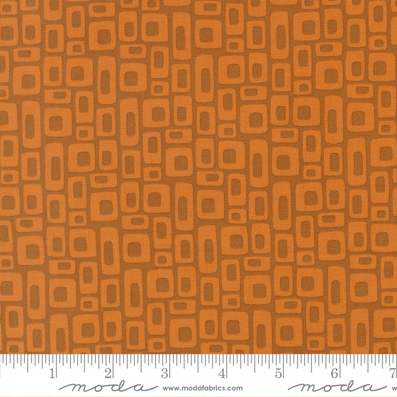 Patterned fabric with geometric shapes on a brown background, featuring a ruler at the bottom for scale.