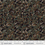 A close-up of a woodland camouflage fabric pattern with green, brown, black, and beige leaf-like shapes, shown with a measuring ruler along the bottom edge from Windham Fabrics.