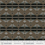A repeating geometric fabric pattern in earthy tones, featuring horizontal bands with diamonds, triangles, and stepped motifs in brown, gray, black, and beige. A ruler scale and Windham Fabrics branding are visible along the bottom edge.