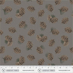 A repeating fabric pattern featuring pinecones and small pine needles on a solid taupe-gray background, with a printed ruler scale and Windham Fabrics branding along the bottom edge.
