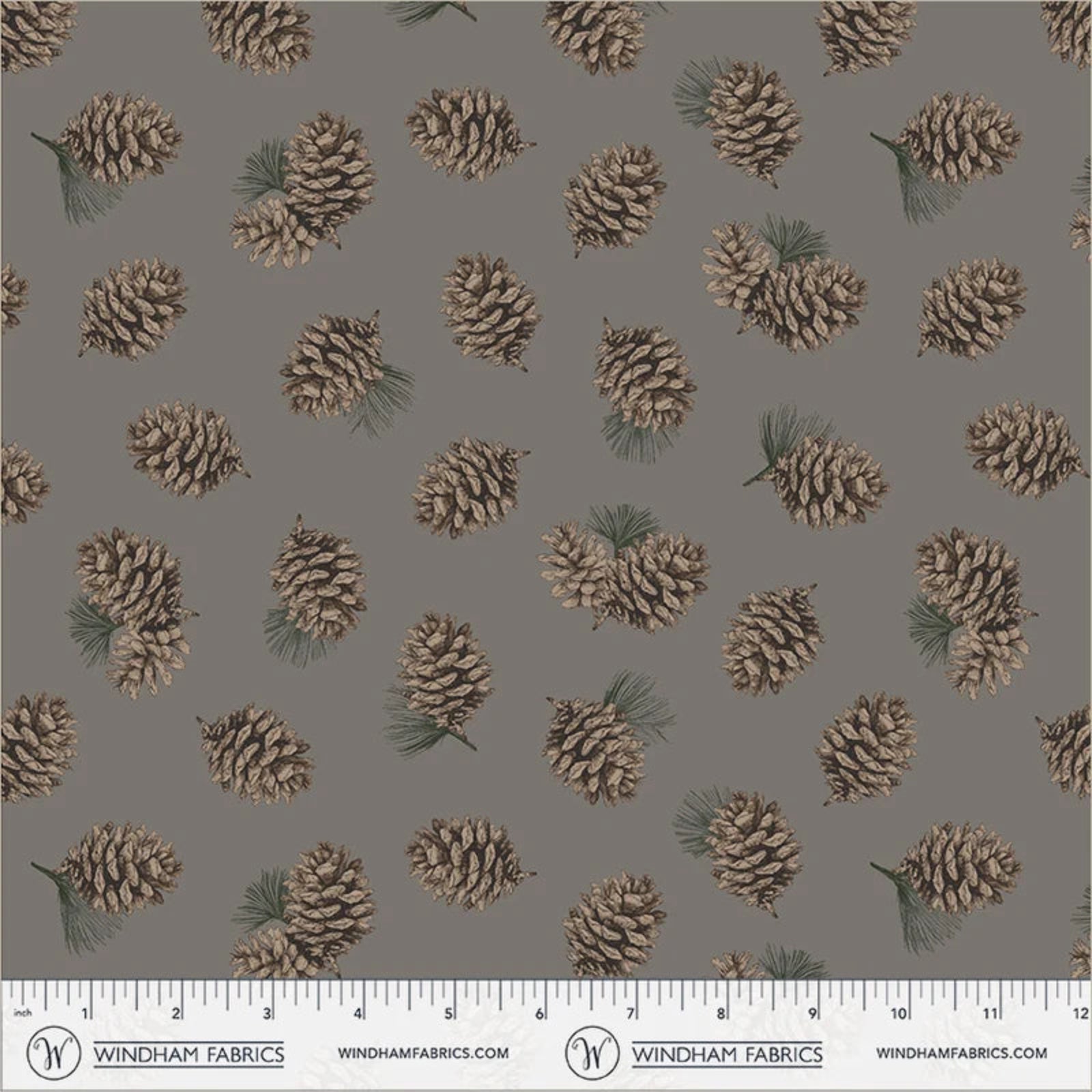A repeating fabric pattern featuring pinecones and small pine needles on a solid taupe-gray background, with a printed ruler scale and Windham Fabrics branding along the bottom edge.