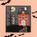 Halloween-themed quilt with a haunted house, witch, and ghosts on a pink background.