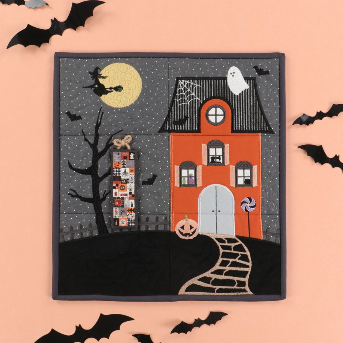 Halloween-themed quilt with a haunted house, witch, and ghosts on a pink background.