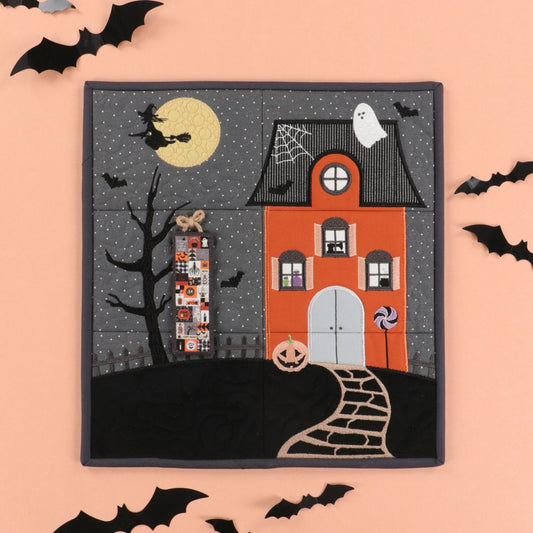 Halloween-themed quilt with a haunted house, witch, and ghosts on a pink background.