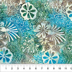 A close-up of a batik fabric with a tropical floral and leaf pattern in shades of teal, blue, green, and brown, featuring a white ruler at the bottom edge for scale.