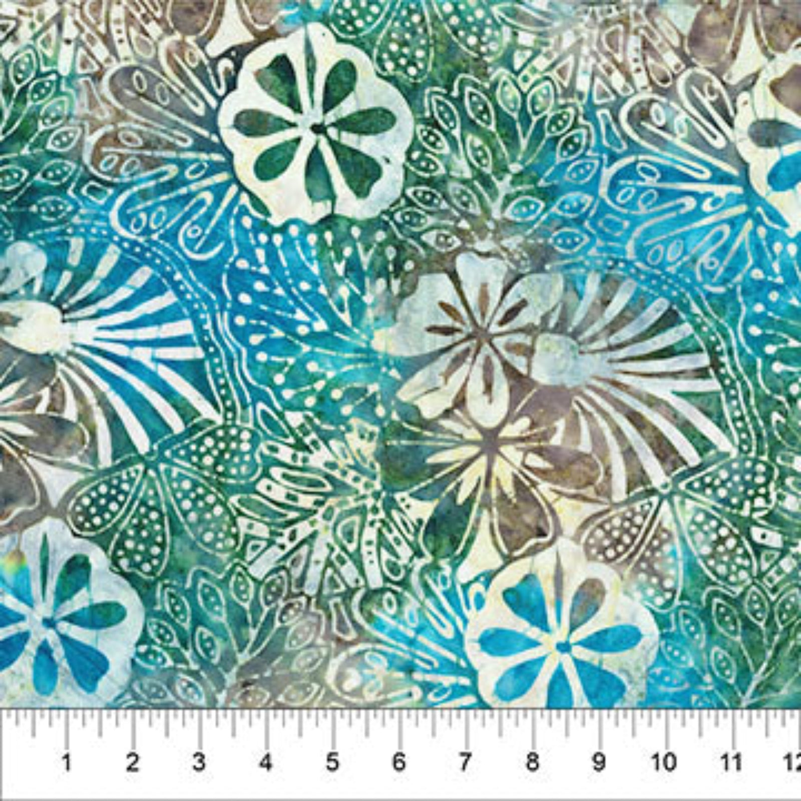 A close-up of a batik fabric with a tropical floral and leaf pattern in shades of teal, blue, green, and brown, featuring a white ruler at the bottom edge for scale.