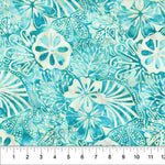 A close-up of a batik fabric pattern featuring teal, turquoise, and off-white tropical floral and leaf motifs, with a white ruler at the bottom showing the scale.