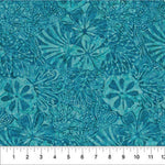 A close-up of a teal and turquoise batik fabric with a repeating floral and leaf pattern, featuring a white ruler at the bottom edge for scale.