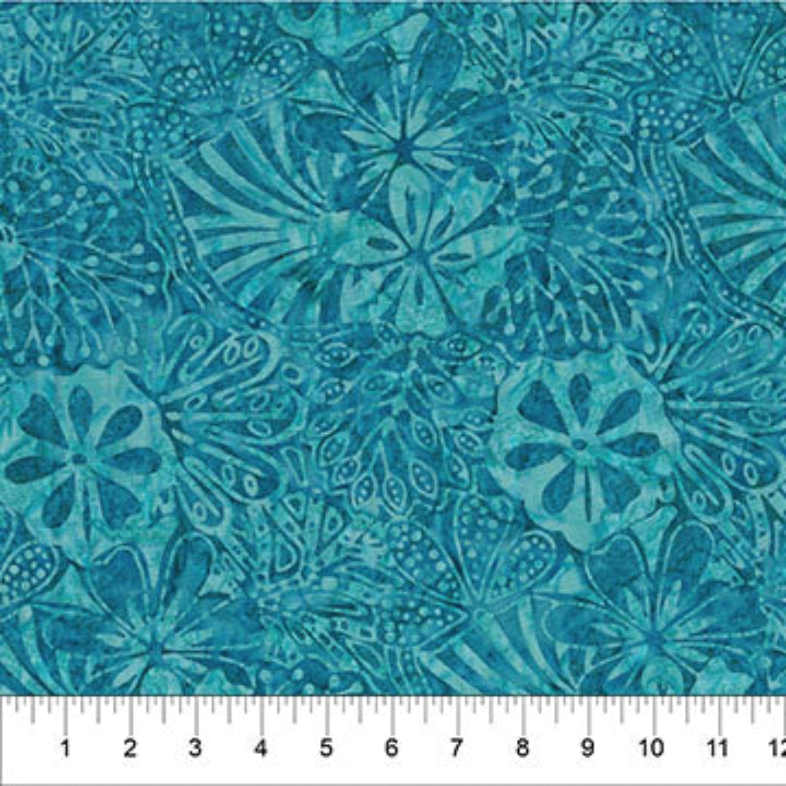 A close-up of a teal and turquoise batik fabric with a repeating floral and leaf pattern, featuring a white ruler at the bottom edge for scale.
