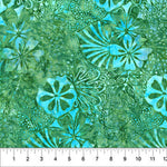 A close-up of a batik fabric with a tropical floral pattern in shades of green and turquoise, featuring a white ruler at the bottom edge for scale.