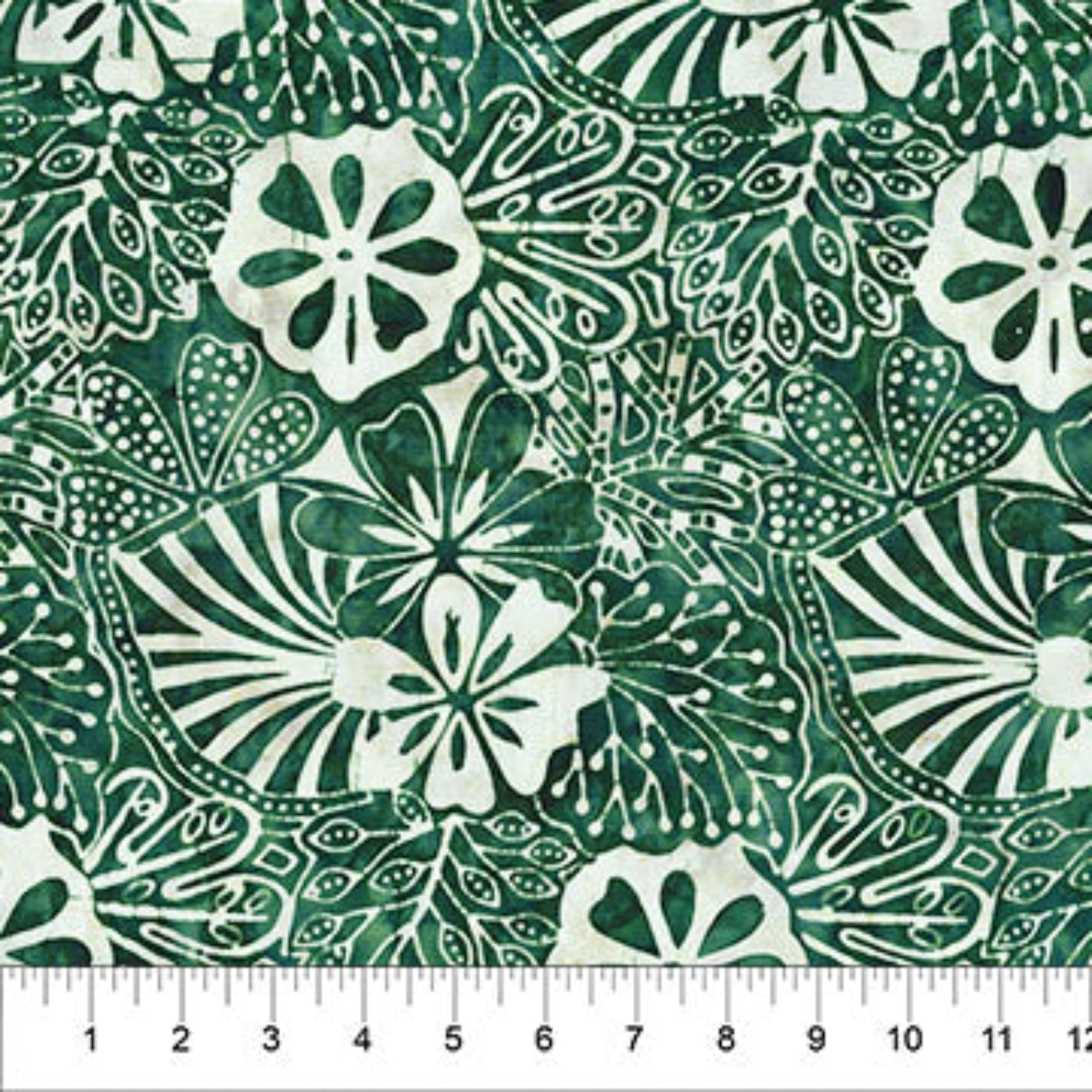 A close-up of a green and white batik fabric pattern featuring stylized floral and leaf motifs, with a white ruler at the bottom showing measurement markings.