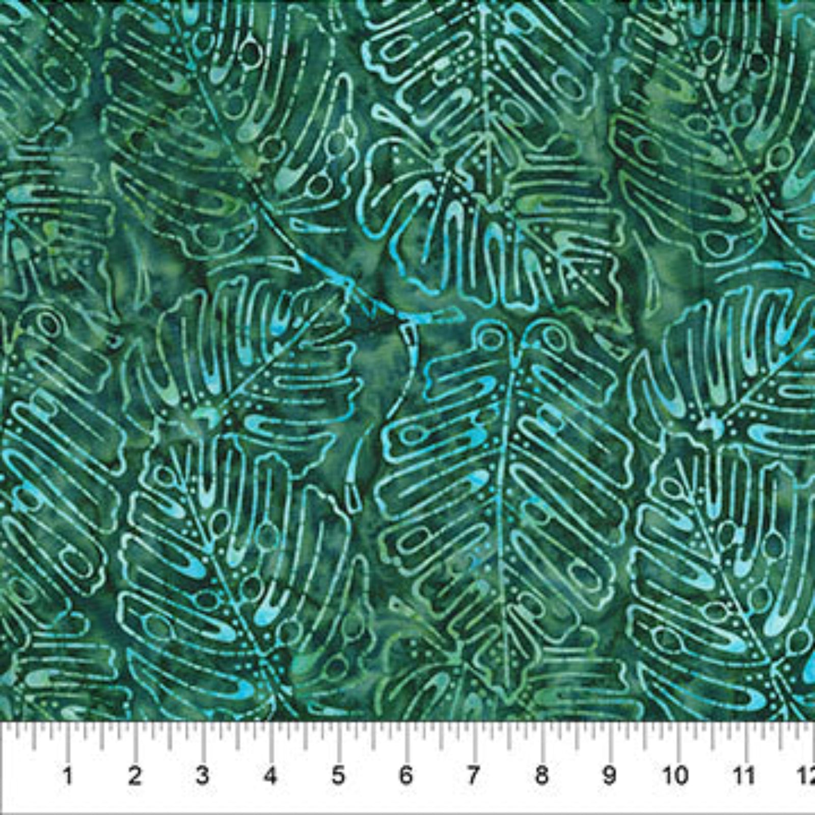 A close-up of a batik fabric with a repeating tropical leaf pattern in shades of green, teal, and turquoise, with a white ruler at the bottom indicating scale.