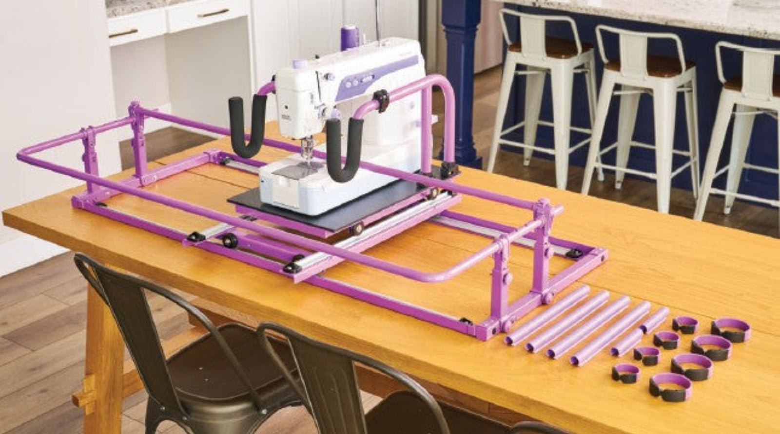 A white and purple sewing machine mounted on a purple metal guide rail system on a wooden table, with matching accessories and small circular pieces arranged beside it. 