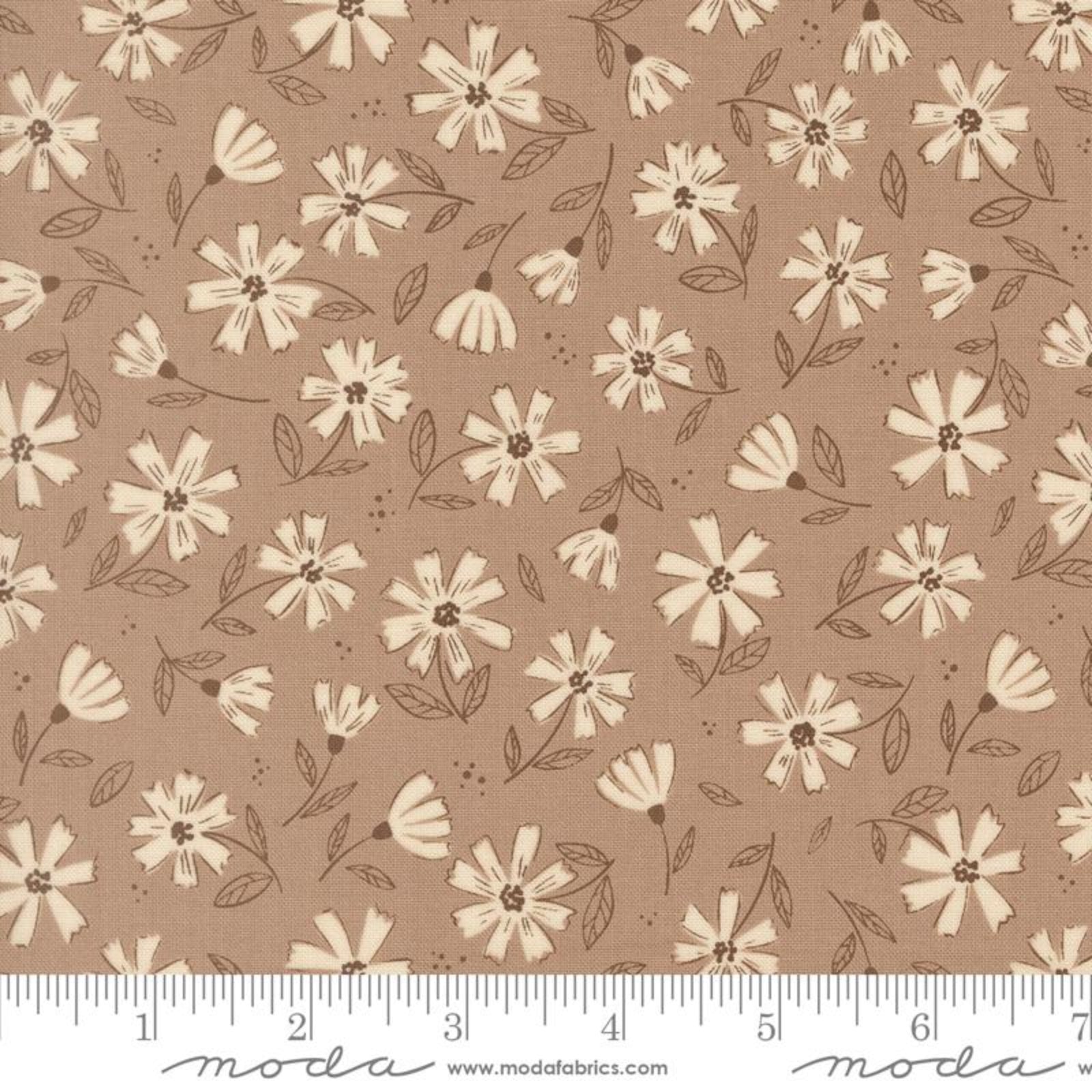 Brown fabric with a repeating cream and beige floral pattern, shown flat with a ruler along the bottom edge for scale. The brand name 'Moda' is visible in script along the bottom.