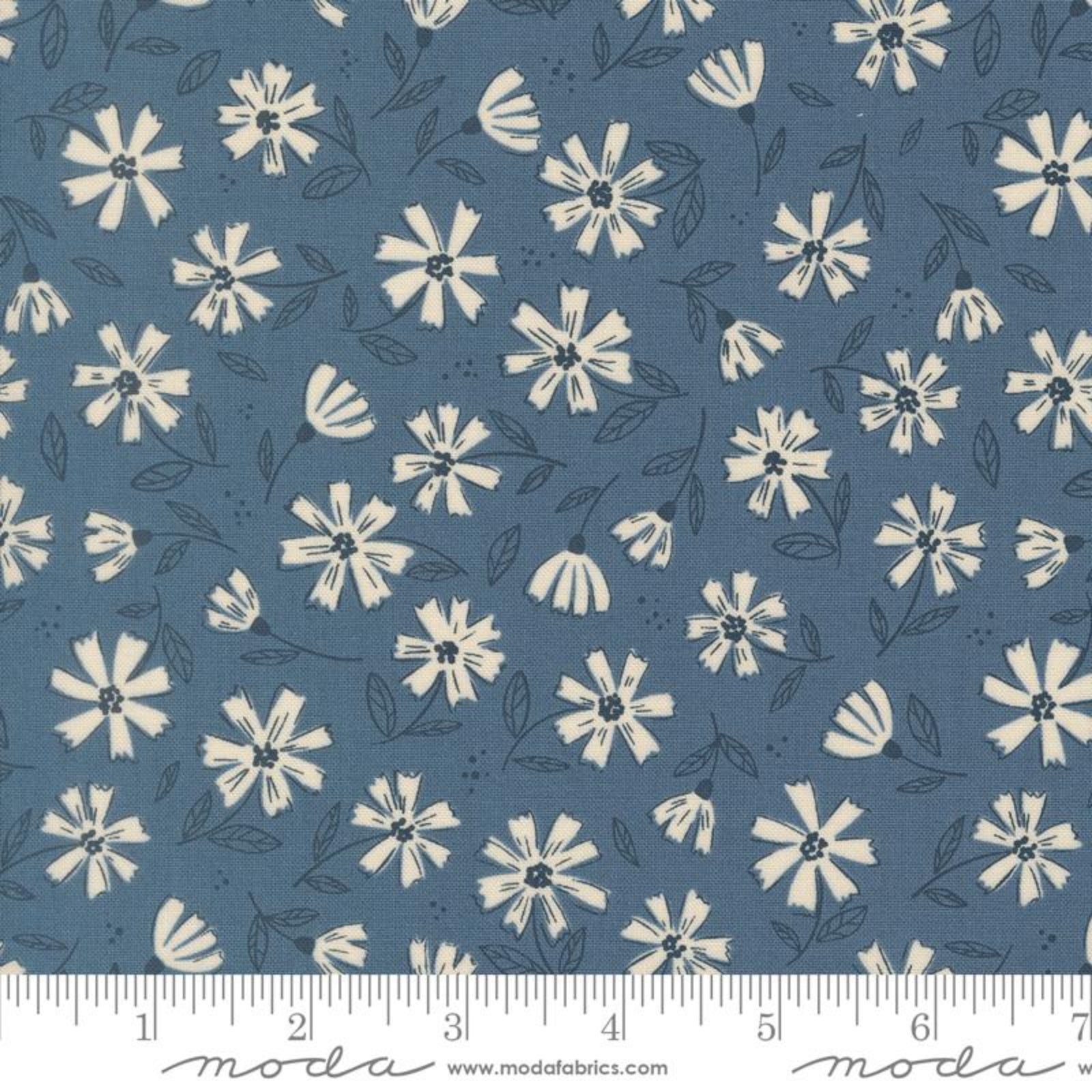 A close-up of a fabric pattern featuring cream-colored daisy-like flowers and dark gray leaves on a muted slate blue background, with a ruler along the bottom edge showing scale.