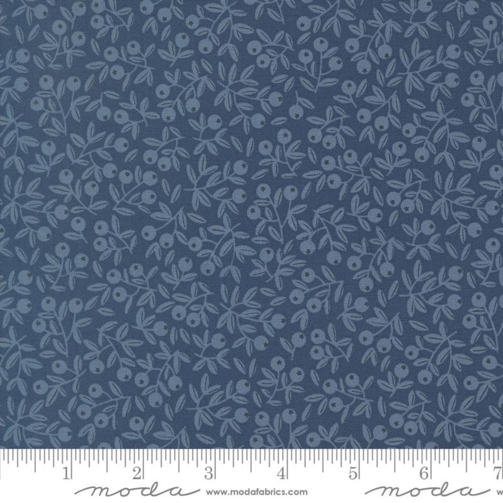 A close-up of a fabric pattern featuring a repeating light blue floral and leaf motif on a medium blue background, with a white ruler along the bottom edge showing scale and Modas Fabrics branding.