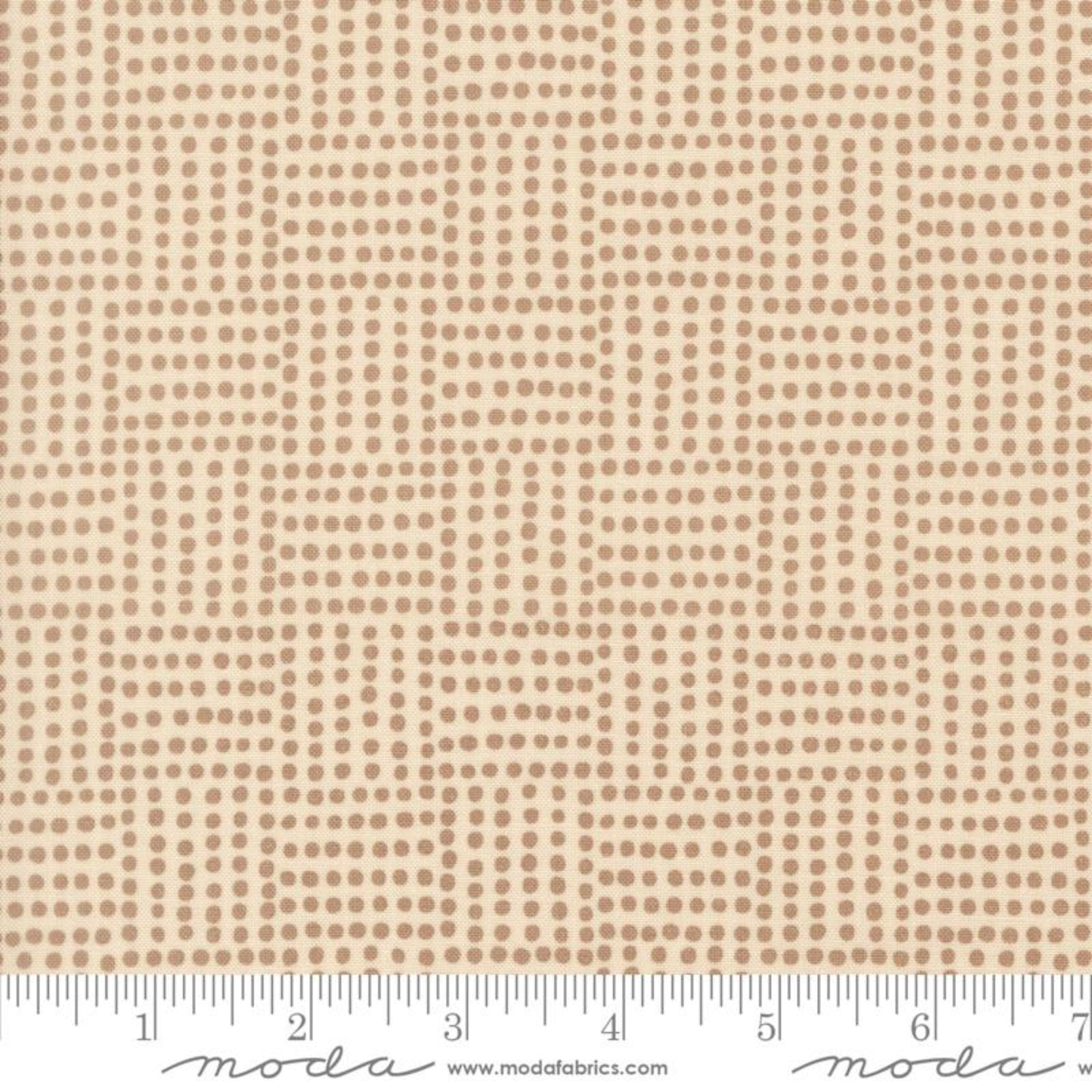 A close-up of a fabric pattern featuring a repeating grid of small brown dots on a warm beige background, with a ruler along the bottom edge and Modas Fabrics branding.