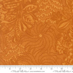 A close-up of orange fabric with a floral and leafy pattern, plus a white ruler along the bottom edge showing measurement markings and the Moda logo.