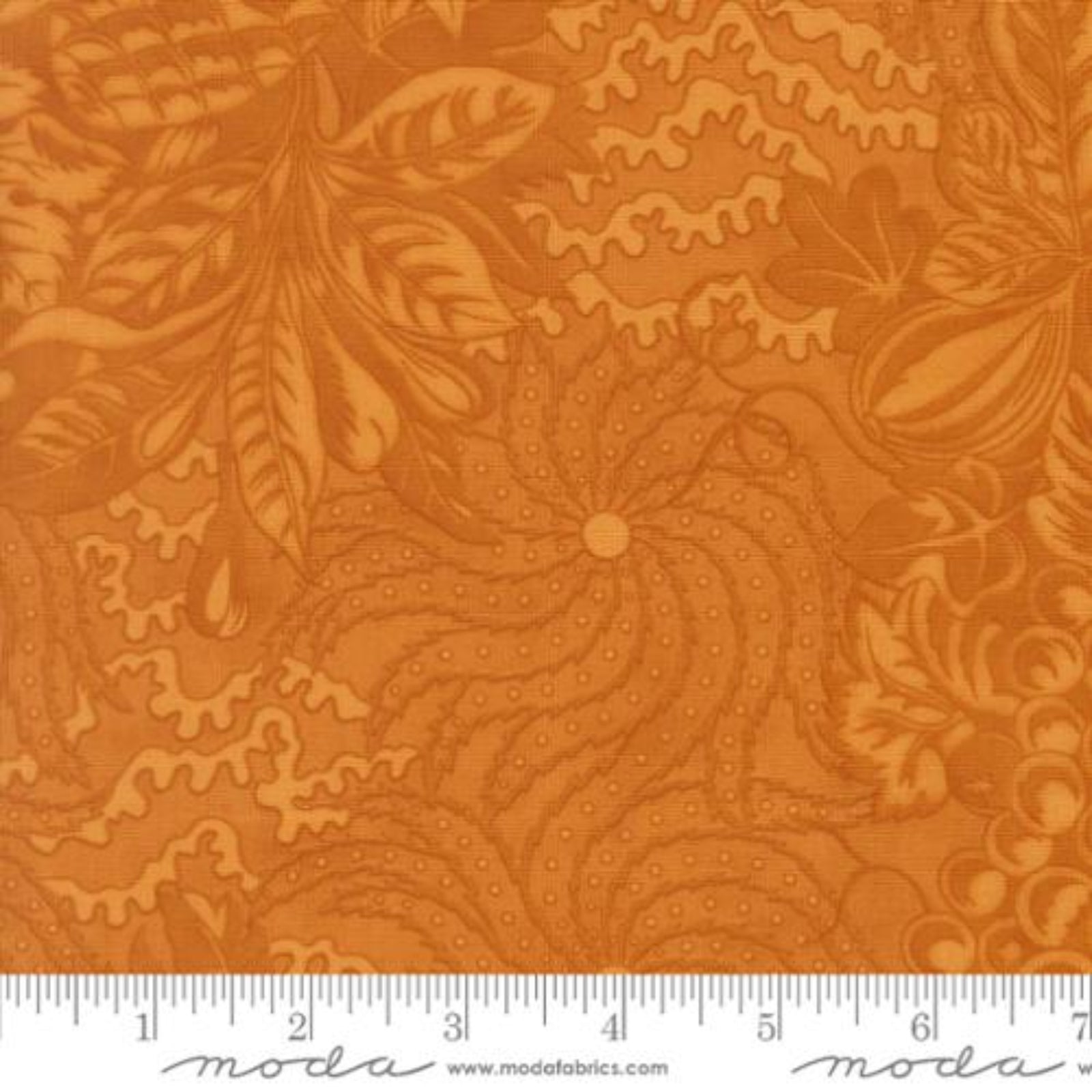A close-up of orange fabric with a floral and leafy pattern, plus a white ruler along the bottom edge showing measurement markings and the Moda logo.