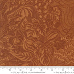 A close-up of a brown fabric with an embossed or printed autumnal pattern featuring pumpkins, gourds, grapes, and leaves. A white ruler along the bottom edge shows scale, and the word 'moda' appears at the bottom.