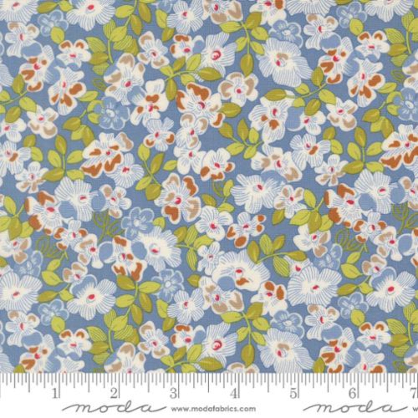 A close-up of a floral fabric pattern with white flowers, green leaves, and small orange-red centers on a dusty blue background, with a measuring ruler along the bottom edge and Modas fabric branding at the bottom.
