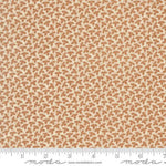 A close-up of a fabric pattern featuring small brown leaves on a warm beige background, with a measuring ruler along the bottom edge showing scale. The brand name 'Moda Fabrics' is visible at the bottom.