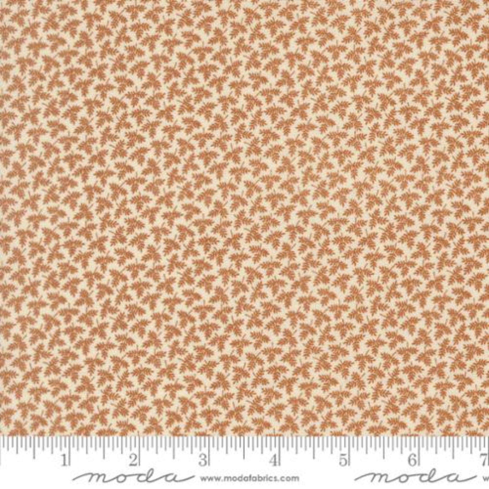 A close-up of a fabric pattern featuring small brown leaves on a warm beige background, with a measuring ruler along the bottom edge showing scale. The brand name 'Moda Fabrics' is visible at the bottom.