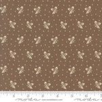 Brown fabric with a repeating pattern of cream bows, small bows, and tiny dots, shown with a white ruler along the bottom edge.