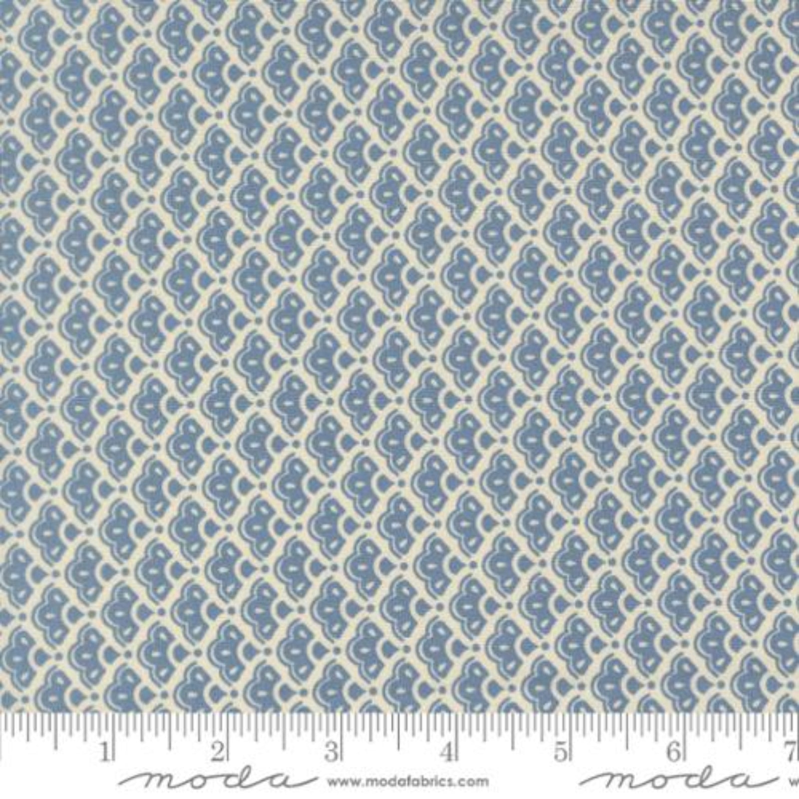 A close-up of a fabric pattern featuring a repeating blue and cream ikat or medallion design, with a ruler at the bottom indicating scale. The brand name 'Moda Fabrics' is visible at the bottom.