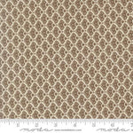 A close-up of a fabric pattern with a repeating brown paisley-like motif on a warm beige background, with a ruler along the bottom edge and Modas Fabrics branding at the bottom.