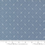 A close-up of a blue fabric with a repeating white geometric diamond pattern, shown with a ruler along the bottom edge for scale. The brand name 'Moda Fabrics' is visible at the bottom.