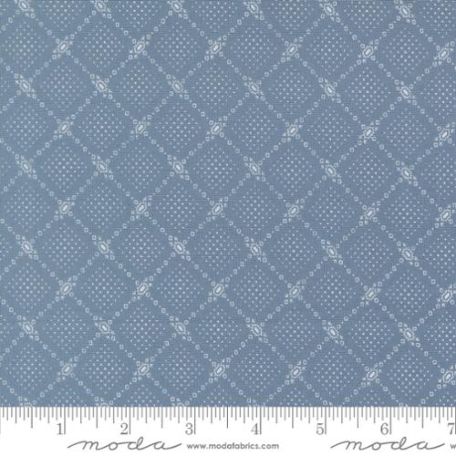 A close-up of a blue fabric with a repeating white geometric diamond pattern, shown with a ruler along the bottom edge for scale. The brand name 'Moda Fabrics' is visible at the bottom.