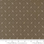 A close-up of a fabric pattern showing a repeating diamond lattice design in warm brown and beige, with a white ruler along the bottom edge and Modas Fabrics branding.